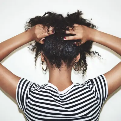 Rearview studio shot of a woman lifting her natural hair off of her neck