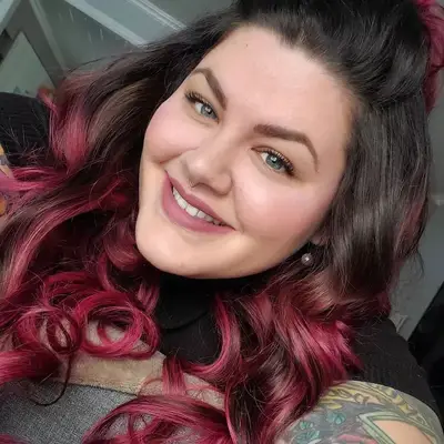 Woman wears long, curled pink ombré hair with dark roots