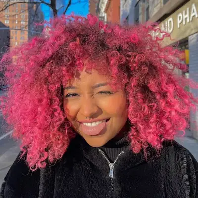 Woman wears vibrant magenta ombré natural curls