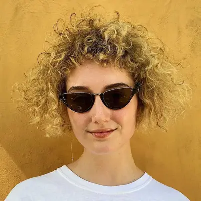 Person with short blonde curls cut in triangle shape and baby bangs