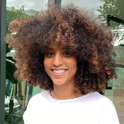 Woman with curly 4a-4b hairstyle with highlights and bangs