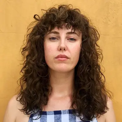 Person with a long, curly brunette shag haircut with bangs