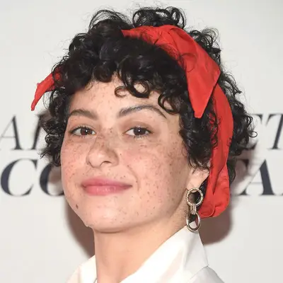 Alia Shawkat wearing short, curly hair with bangs and a vintage red ribbon headband at the 2018 