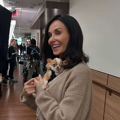 Demi Moore smiling and holding a small dog indoors