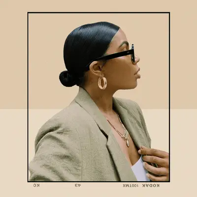 side profile of a woman with slicked back bun, sunglasses, and a green jacket.