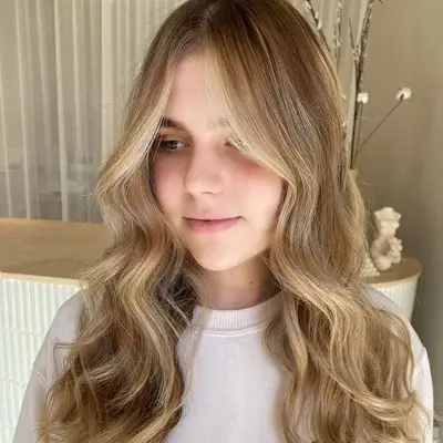 Woman wears soft blonde wavy hair with a face-framing balayage