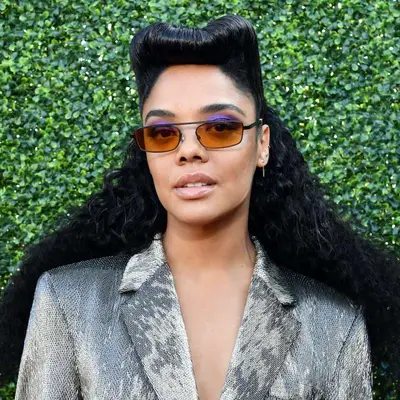 Tessa Thompson wears a victory rolls hairstyle and orange sunglasses