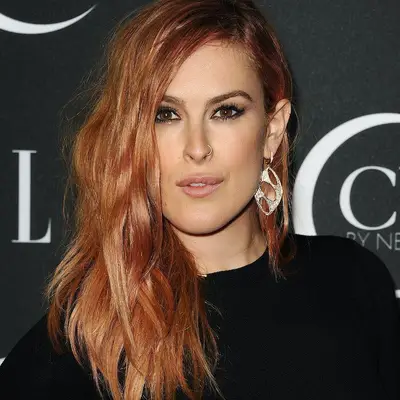 Rumer Willis in black top with statement earrings and deep peach rose gold hair