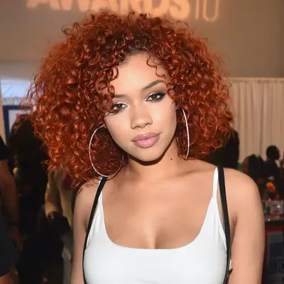 Woman wears a curly red bob hairstyle and large silver hoop earrings