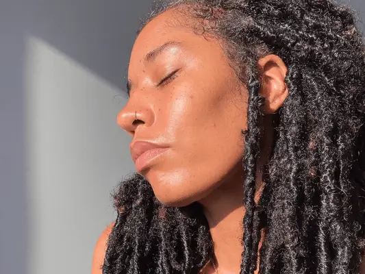 A woman with the sun hitting her face and locs in her hair