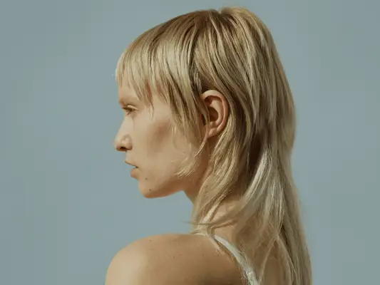 A close up, side profile of a model with a blonde mullet.