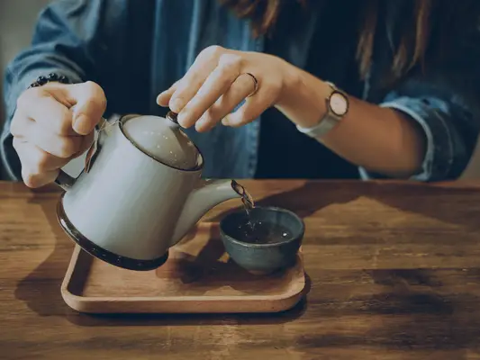 Hands holding a tea pot and pouring tea into a smaller cup