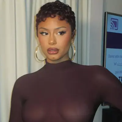 Jorja Douglas with short curly hair wearing a high-neck top, posing indoors