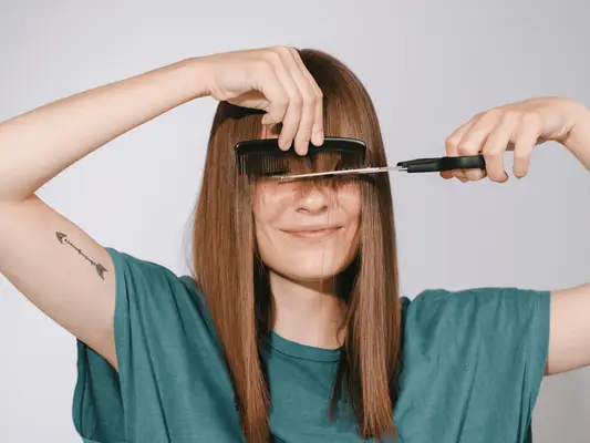 A woman with a comb and a scissor in front of her face as she trims her bangs