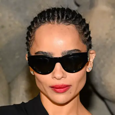 Zoe Kravitz with thin goddess braids pulled back into tiny low bun wearing black sunglasses and red lipstick