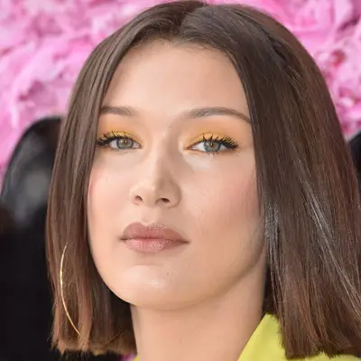 Bella Hadid wears a blunt bob haircut, yellow eyeshadow, and large hoop earrings