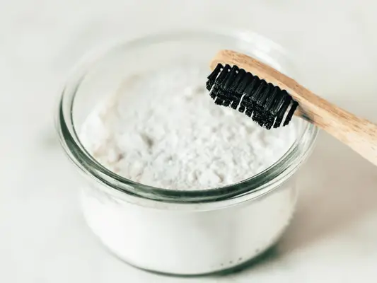 A bowl of baking soda with a black bristle toothbrush propped up on the side