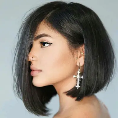 Woman with an asymmetrical A-line bob haircut, silver jewelry, and winged eyeliner