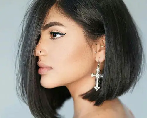 Side view of woman with asymmetrical A-line bob haircut, silver jewelry, and winged eyeliner