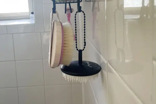 Jupiter Scalp Brush hanging from hook in shower near another brush