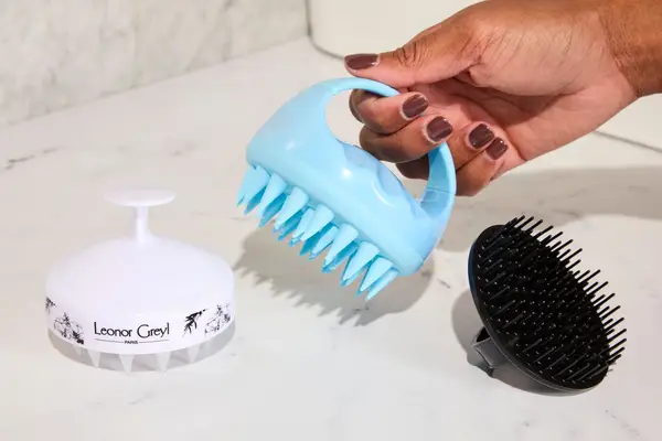 A hand holds a scalp massager with two other massagers nearby on a counter