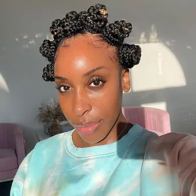 Jackie Aina wears a braided Bantu knot hairstyle and blue tie-dye sweatshirt