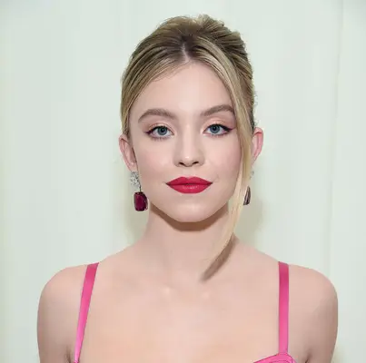 Sydney Sweeney wears a bright pink bra strap dress, punchy pink lip and large gemstone earrings, with a heavy chunk of hair from her updo framing her face