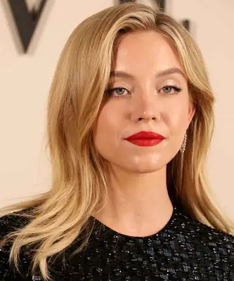 Sydney Sweeney wears softly brushed hair over a sequined black dress and a contrasted bold red lip during Paris Fashion Week