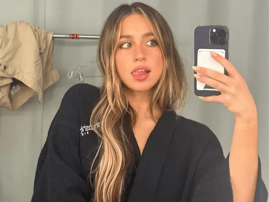 Tate McRae with wavy hair, wearing a robe, and taking a mirror selfie