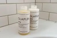 Bottles of Olaplex No. 4 Bond Maintenance Shampoo and Conditioner on the edge of a bathtub