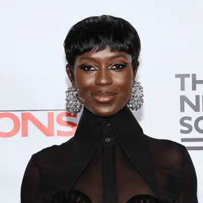 Jodie Turner Smith wearing a black top, chandelier earrings and short black haircut with bang.