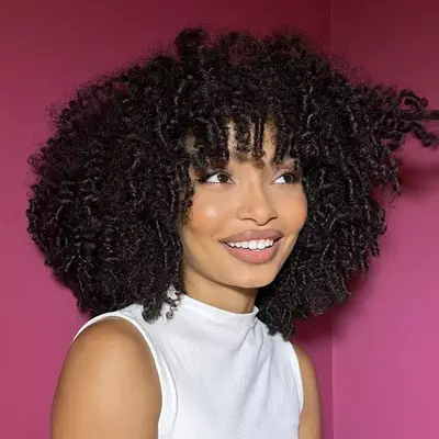 yara shahidi in white shirt with tight springy curls against fuschia background