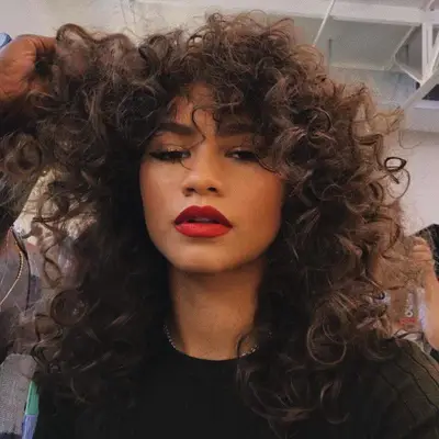 Zendaya wears long, voluminous curly hair with bangs