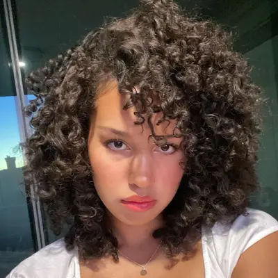 Sofia Wylie wears a voluminous curly hairstyle with side-swept bangs