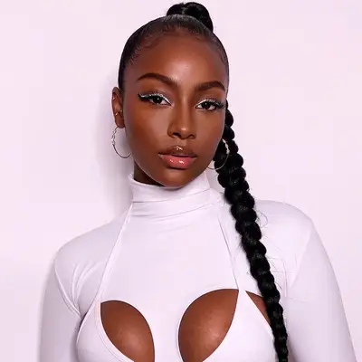 Justine Skye wears a slicked back high ponytail braid, silver eyeliner, and hoop earrings
