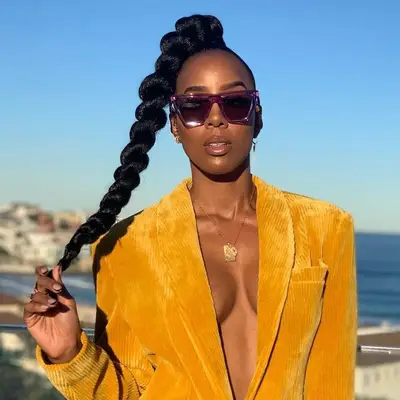 Kelly Rowland wears a jumbo high ponytail braid, yellow corduroy blazer, and large sunglasses