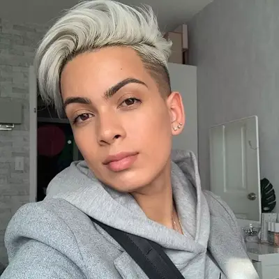 Sabrina Elba wears a long, thick pixie with uneven feathered bangs, red lips and a chunky earring while attending Paris Fashion Week