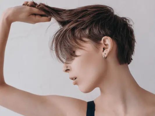 A woman with a short hair cut pulling at the longer pieces with one of her hands