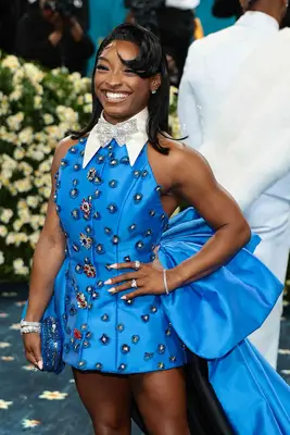 Simone Biles smiling on the red carpet showing off a big, sweeping Betty Boop bang for her 2025 Met Gala look.