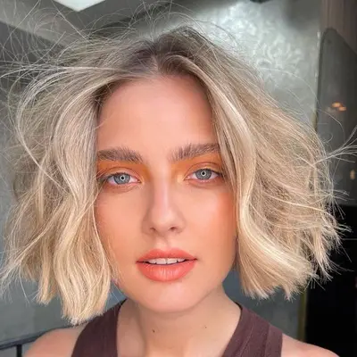 Woman with blonde tousled bob hairstyle and warm-toned makeup