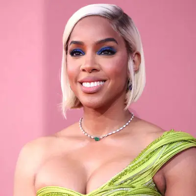 Kelly Rowland smiling in one shoulder green top and side part blonde bob with swoop