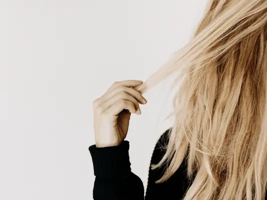 Half of a head of blonde hair with a hand holding a few strands of it