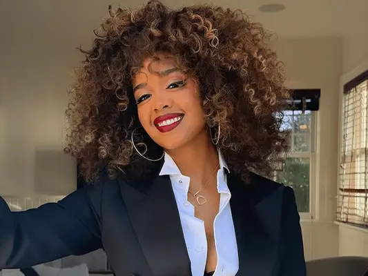 singer H.E.R. with curly hair with caramel highlights