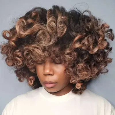 Woman with curly hair and light brown balayage.
