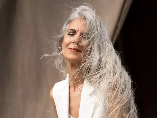 Woman with long white hair in the wind, posing in front of a beige backdrop
