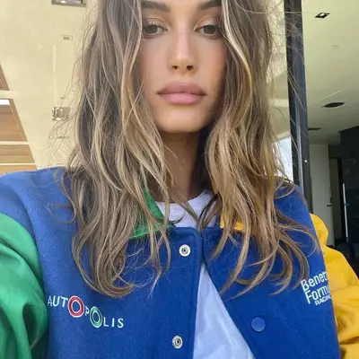 Hailey Bieber wears a varsity jacket and mushroom brown hair with highlights