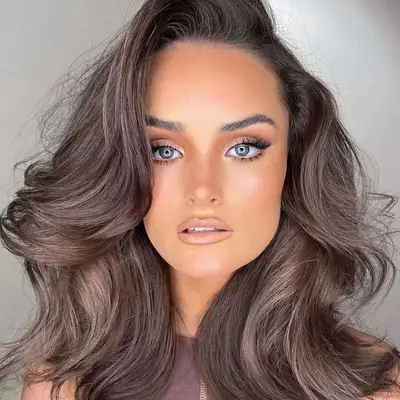 Woman with voluminous, cool-toned dark mushroom brown hair and radiant makeup look