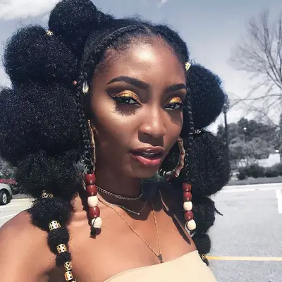 A woman with braids in the front of her hair, the rest in afro puffs with accessories