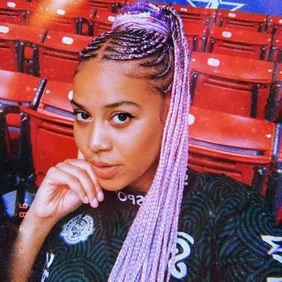 A woman with pink cornrows that go into plaits, piled onto the top of her head in a high ponytail