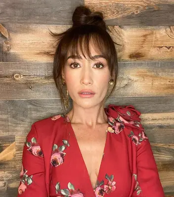 Maggie Q wispy bangs and messy bun in red rose outfit in front of wood wall